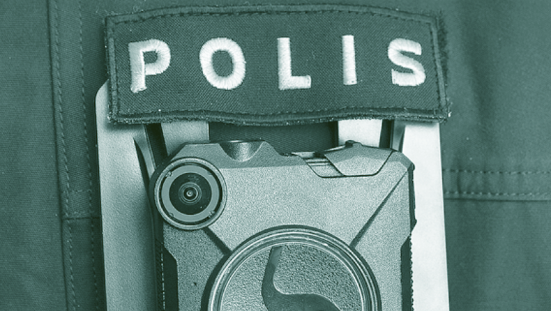 Närbild på en polisuniform med en kroppsburen kamera monterad nedanför ordet Polis.